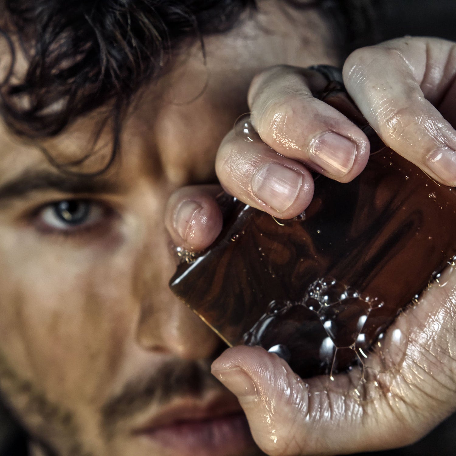 Man holding a glass, evoking the haunting allure of The Cursed Cowboy scent, featuring clove and campfire notes for mystery and allure.