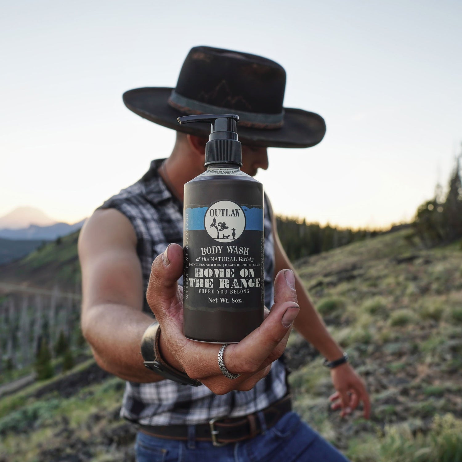 Person holding a Craft Your Own Home on the Range Scent Soundtrack body wash bottle, evoking fresh-cut grass, laundry, and blackberries scent.