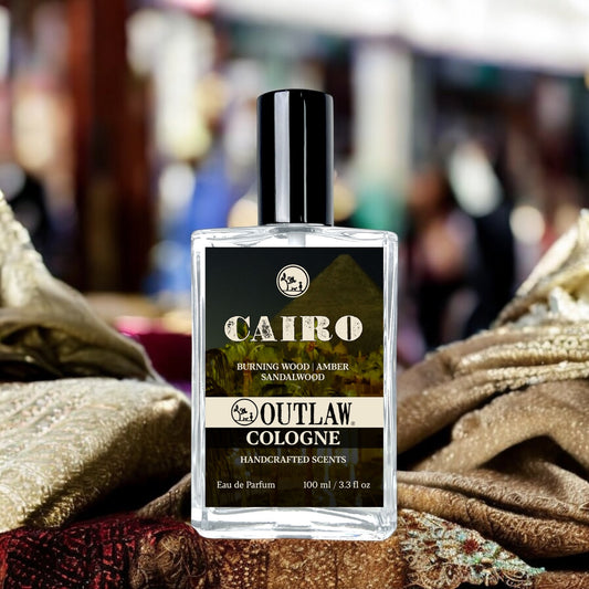 CAIRO Cologne - November's Scent of the Month: A 100 ml transparent bottle featuring a black and white emblem with a dog and tree, resting on textured fabric.