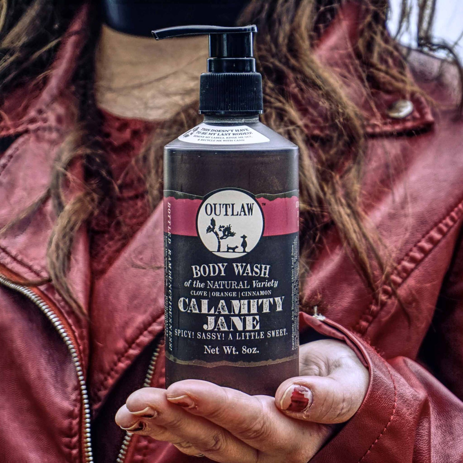 Person holding Craft Your Own Calamity Jane Scent Soundtrack body wash, featuring clove, orange, cinnamon, and whiskey notes for an adventurous scent experience.