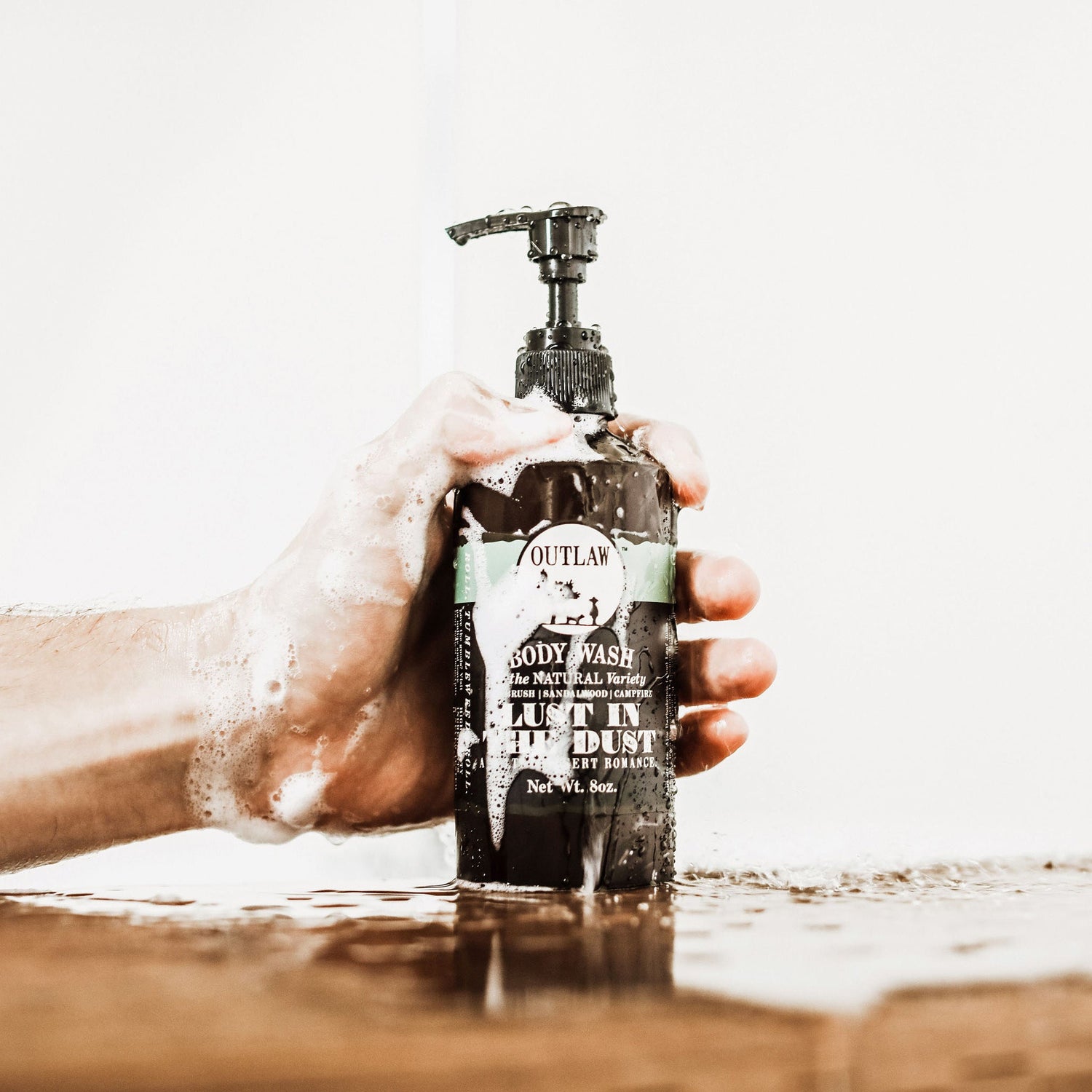 Person holding a Craft Your Own Lust in the Dust Scent Soundtrack soap bottle with a pump, evoking desert scents of sagebrush, sandalwood, and campfire.